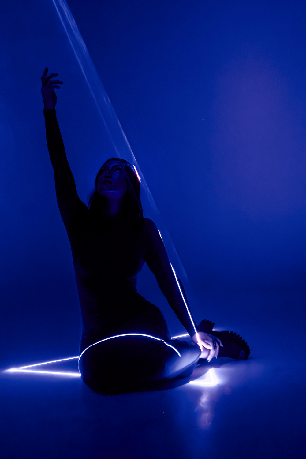 Silhouetted figure in artistic pose with glowing light trails against deep blue background creates dramatic atmosphere.