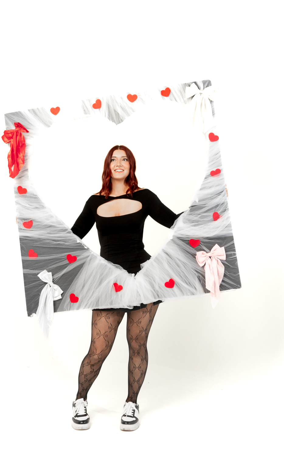 Playful fashion poses in black outfit and tulle skirt with floating red heart graphics against white backdrop.