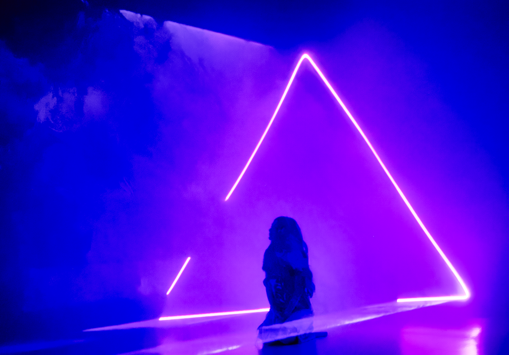 Geometric neon lights in purple and blue creating triangular shapes in dark space.