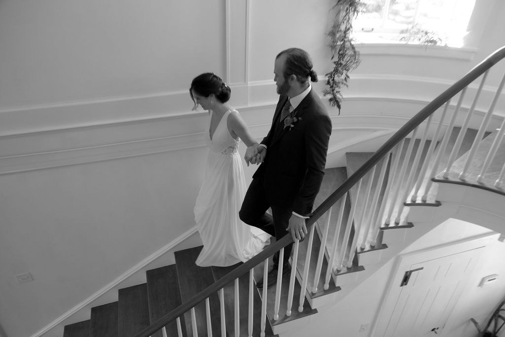 A black and white wedding photo series showing a couple descending an elegant curved staircase in formal attire.