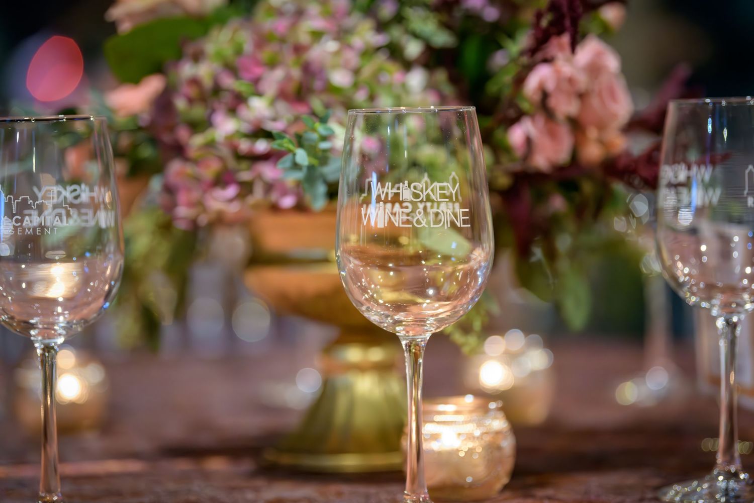 Elegant table setting with wine glasses and soft candlelight illuminating pink floral arrangements at a wedding reception.