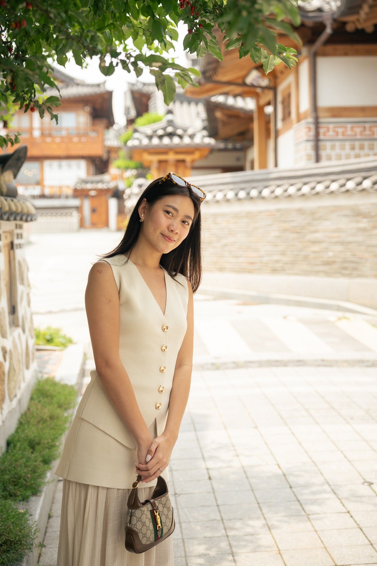 A person in a cream-colored dress poses in front of traditional Korean hanok architecture on a sunny day.