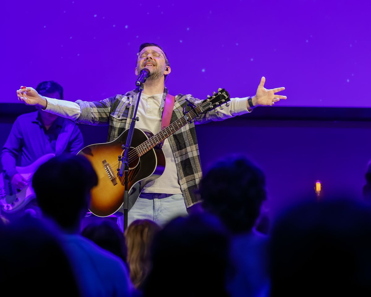Musician performing with acoustic guitar on purple-lit concert stage.