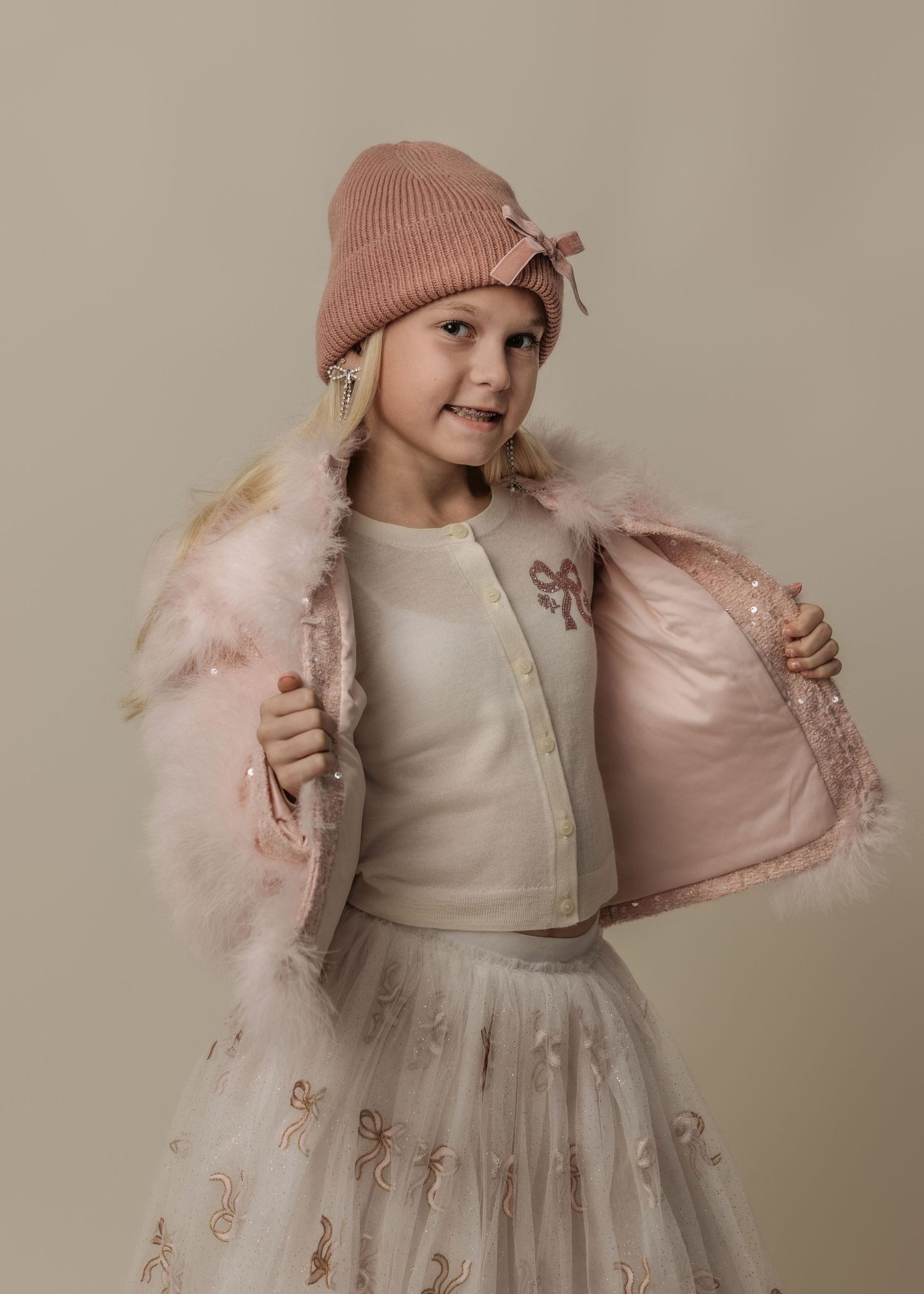 Child modeling photos showcasing a winter outfit with pink beanie and white tulle dress.