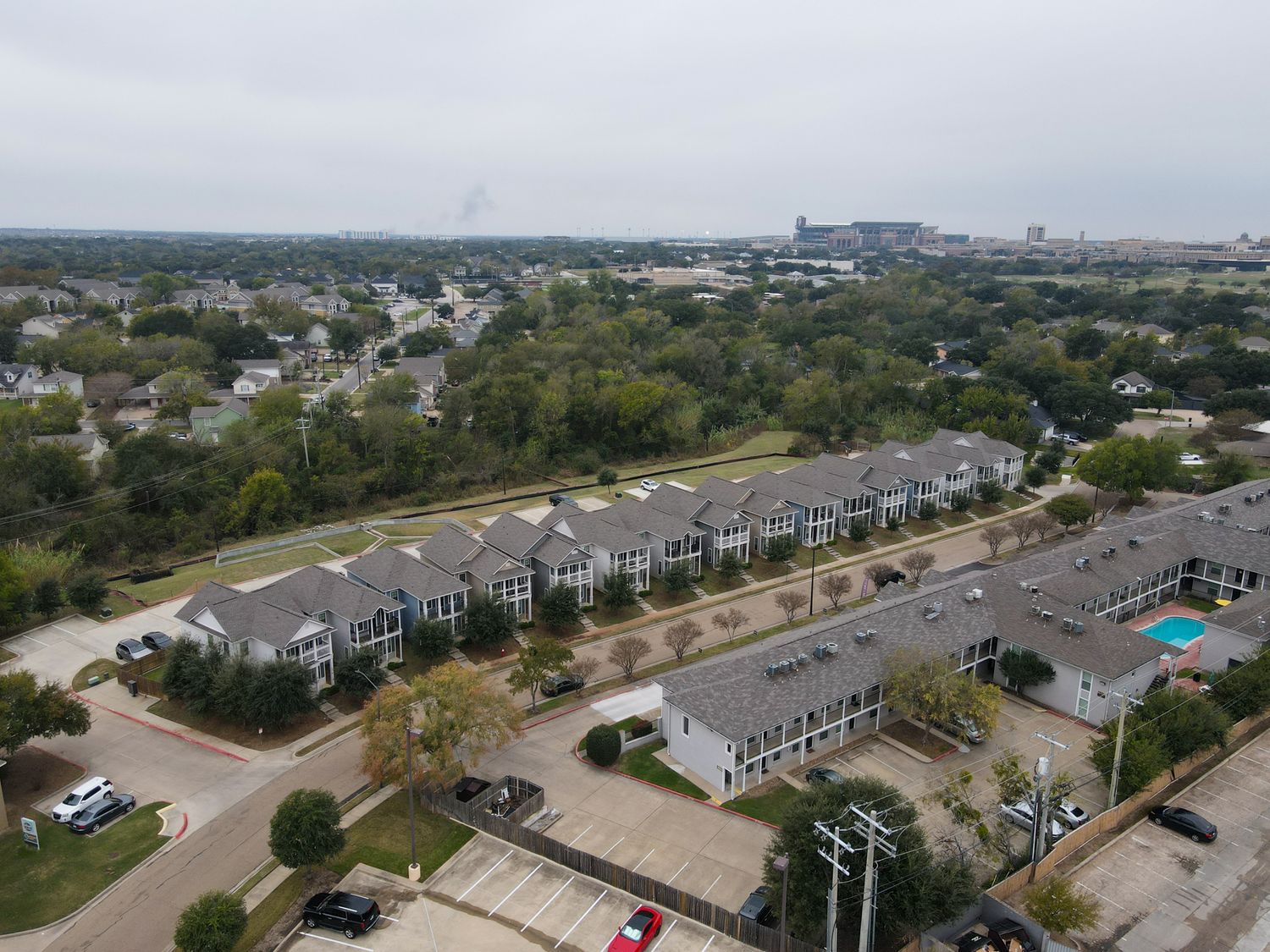 Aerial view of modern townhouse development with gray roofs and parking lots stretching along suburban landscape.