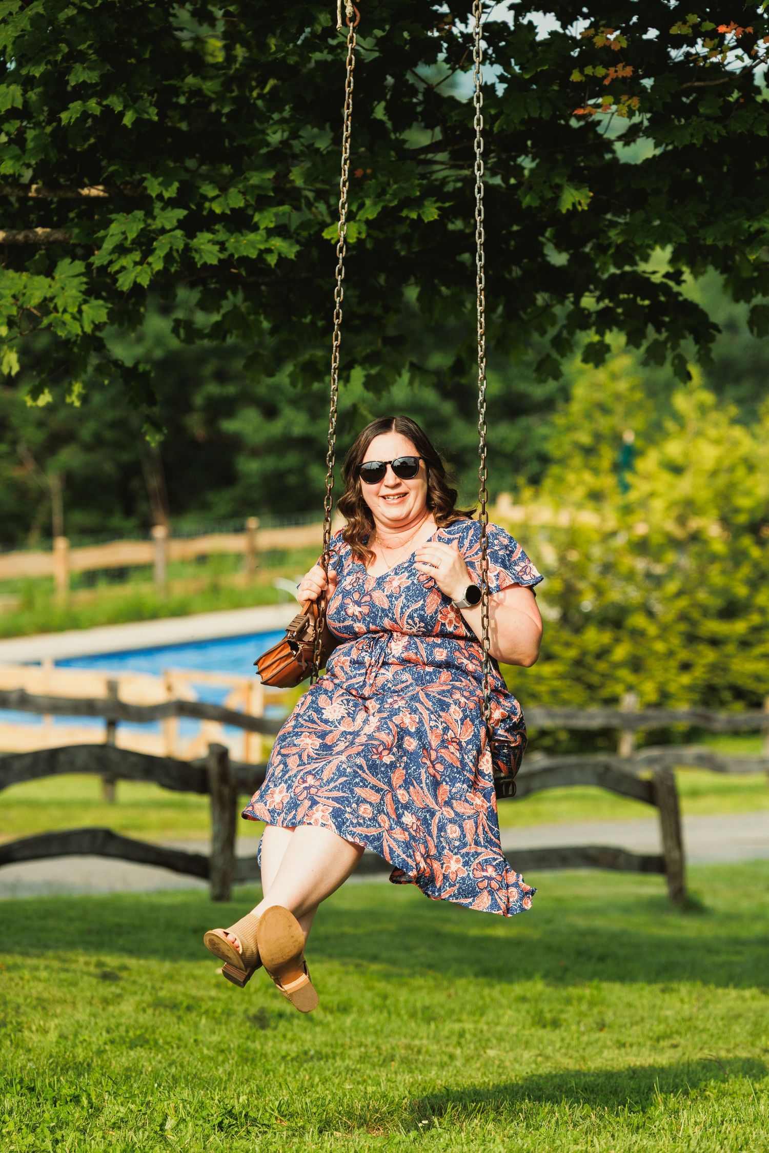 Person in a floral dress enjoys swinging at a garden party with a pool in the background.