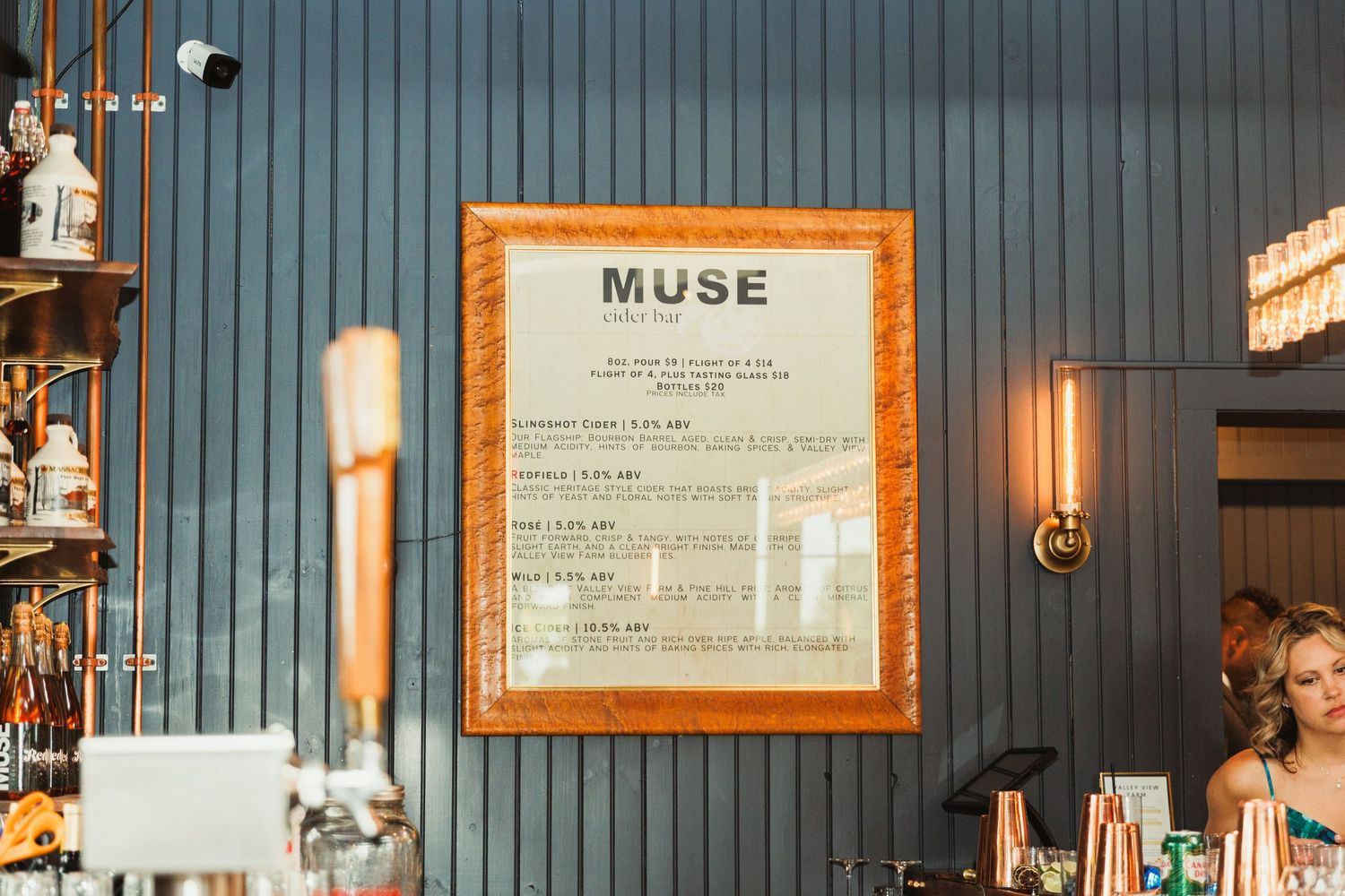 A framed menu titled 'MUSE' hangs on a blue-gray wall in a restaurant or bar setting.