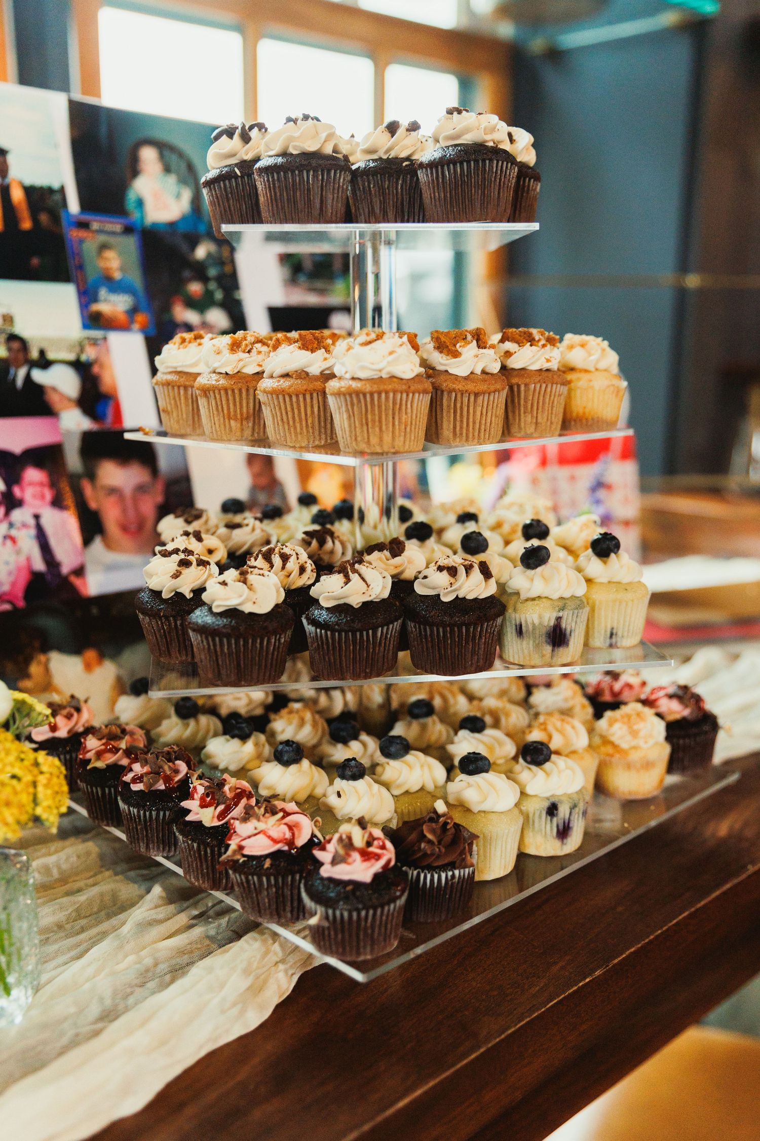 A tiered display of assorted cupcakes with chocolate, vanilla and decorated frosting at an event.