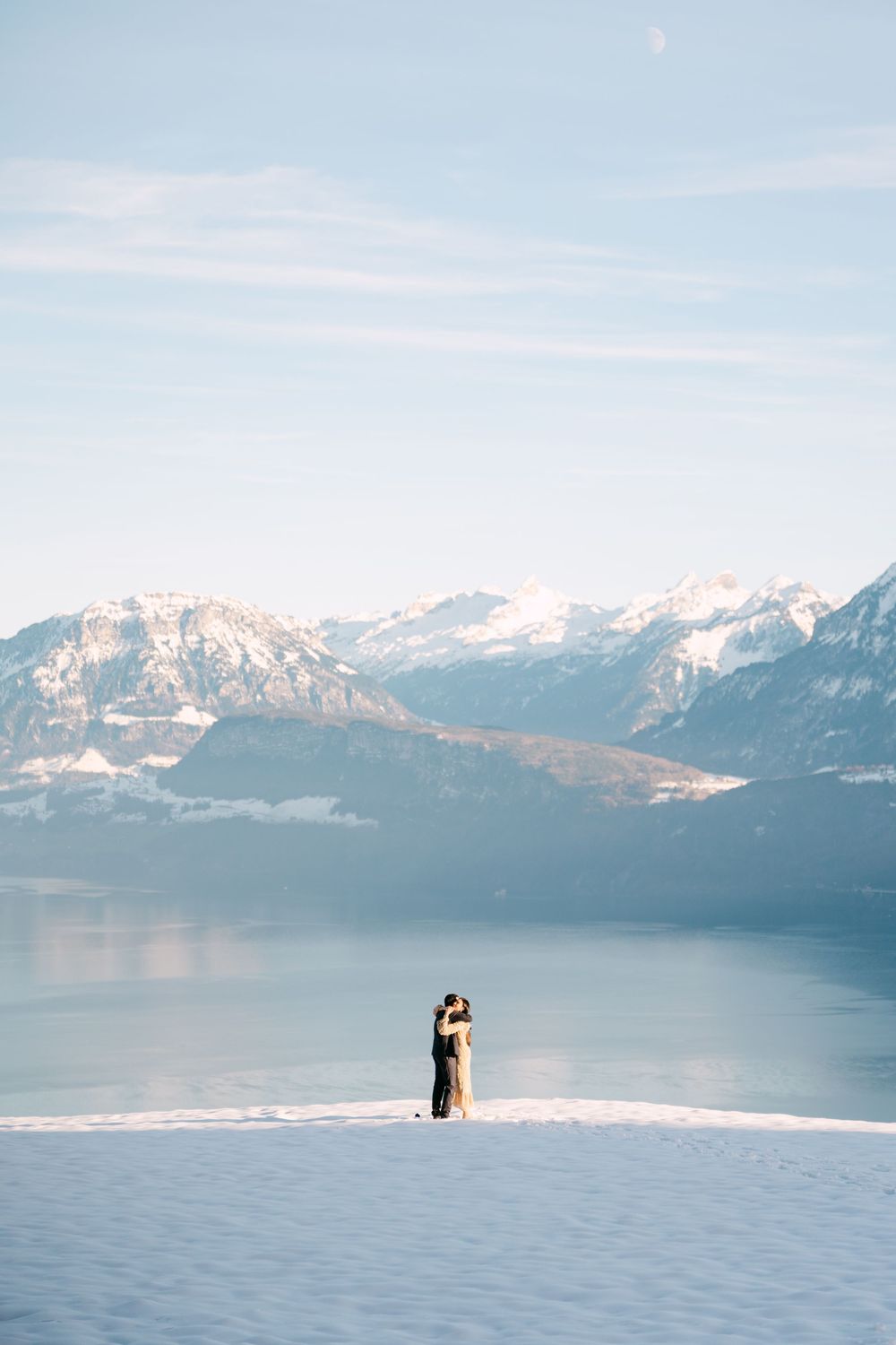 Two silhouettes stand together against a backdrop of snowy mountains and a serene lake in a romantic winter landscape above lake Lucerne.