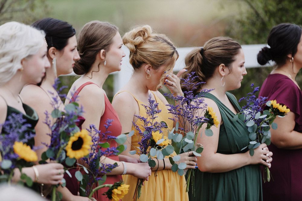 An emotional bridesmaid wipes a tear amid bridesmaids dressed in fall colors during a ceremony in Windham, New Hampshire during autumn.