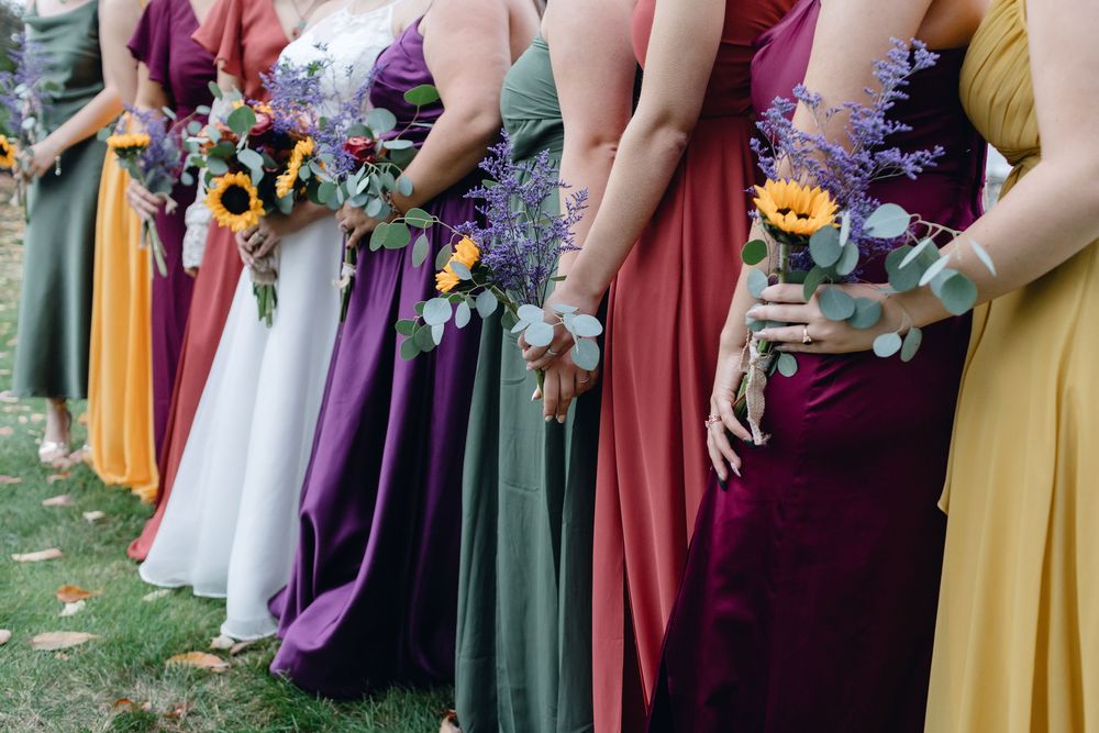A colorful array of bridesmaids dresses and flowers viewed at hip level during a wedding ceremony in Wndham, New Hampshire.