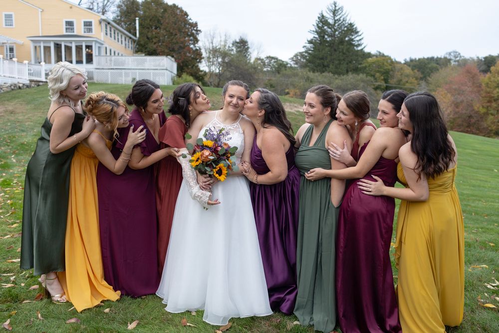 Bridesmaids wearing fall colors gush over the bride holding an autumn colored bouquet at Westbrook Inn in Derry New Hampshire.