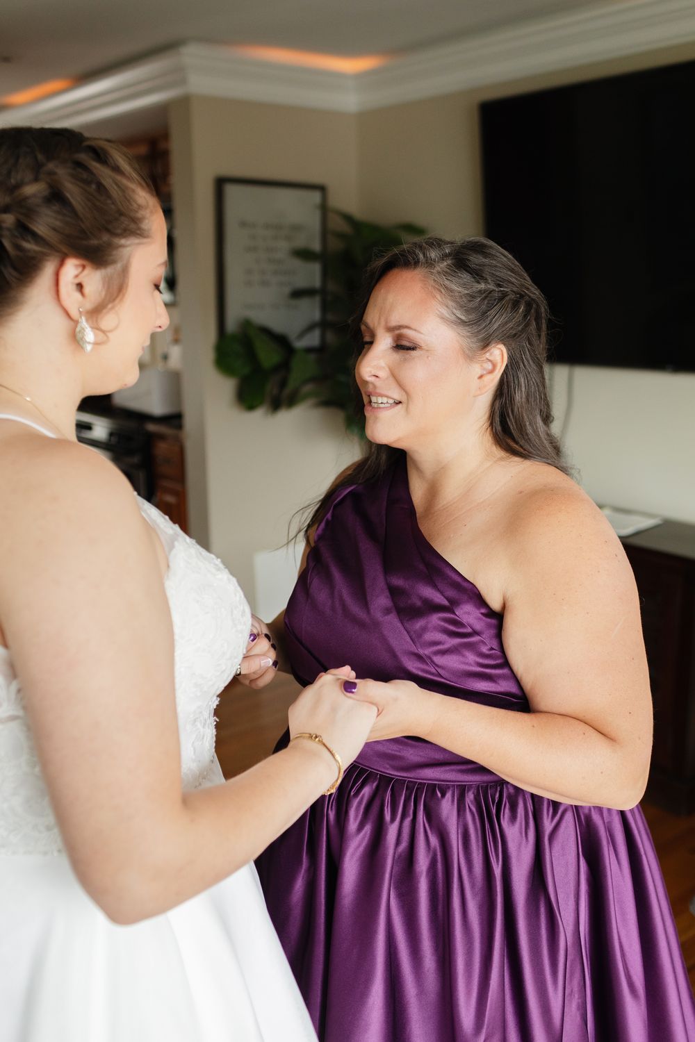 Mother of the bride wearing a purple satin dress prays with bride daughter during for getting ready wedding photos in New Hampshire.