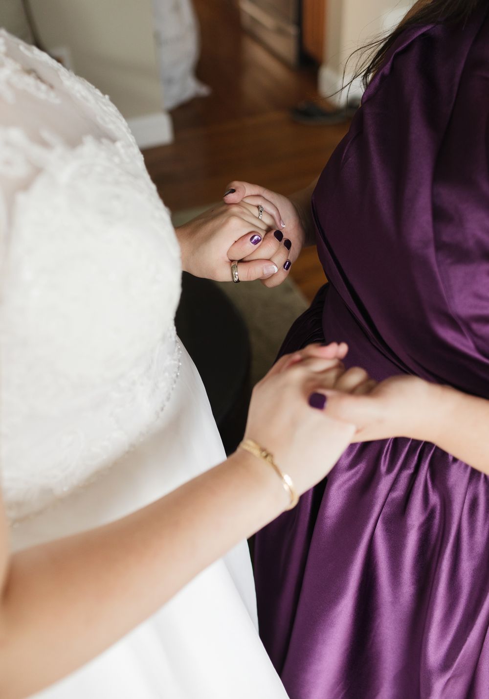 A close up of a mother of the bride wearing purple holds her bride daughter's hand for getting ready photos in Windham, New Hampshire.
