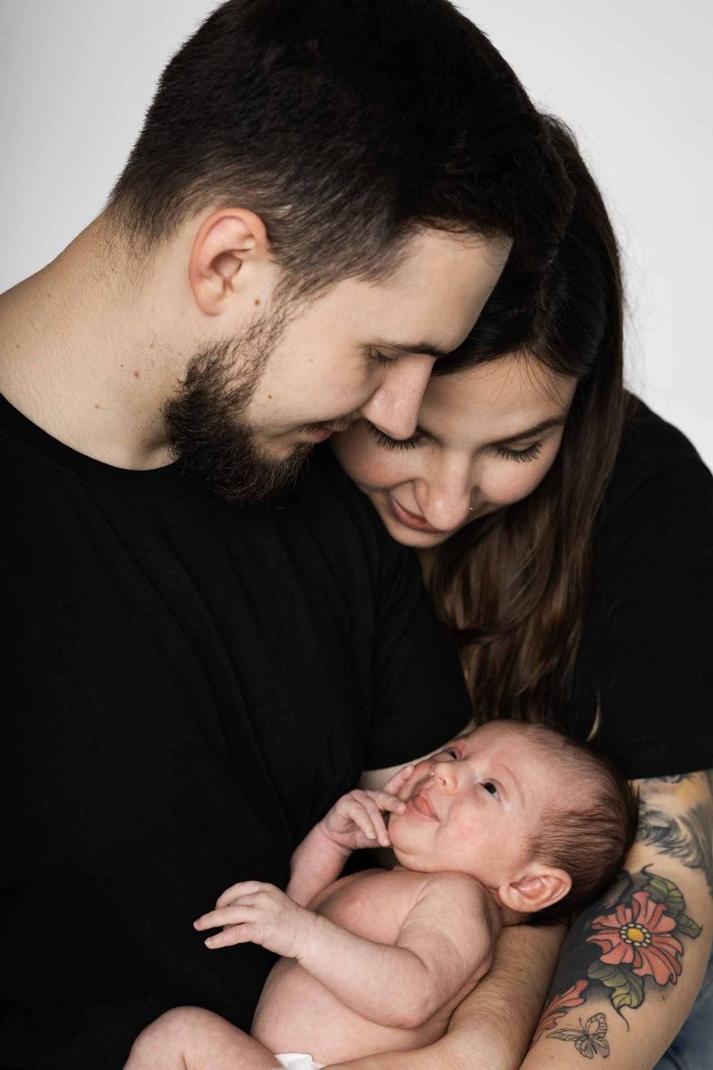 An intimate family portrait showing parents gazing lovingly at their newborn baby.