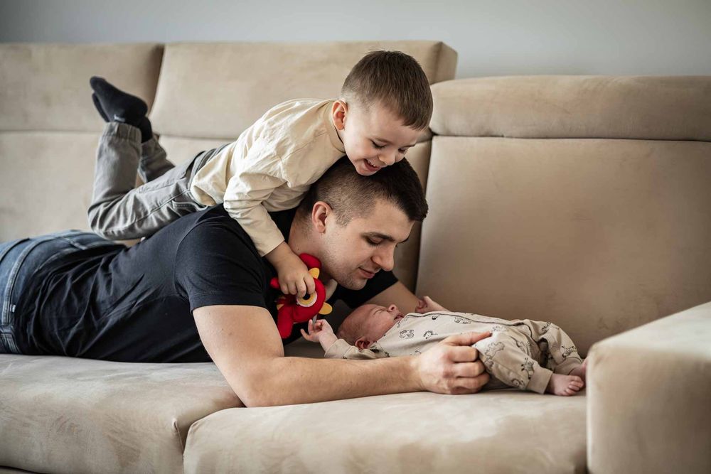 Playful family moment captured on a beige couch with genuine laughter and joy.