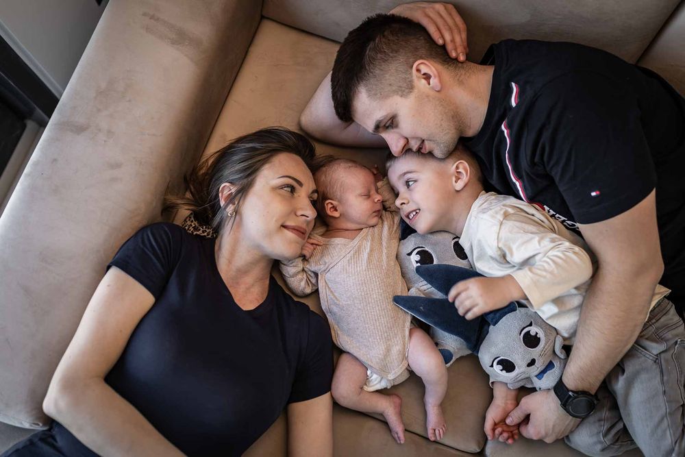 A family cuddles together on a couch with their baby and stuffed toy.