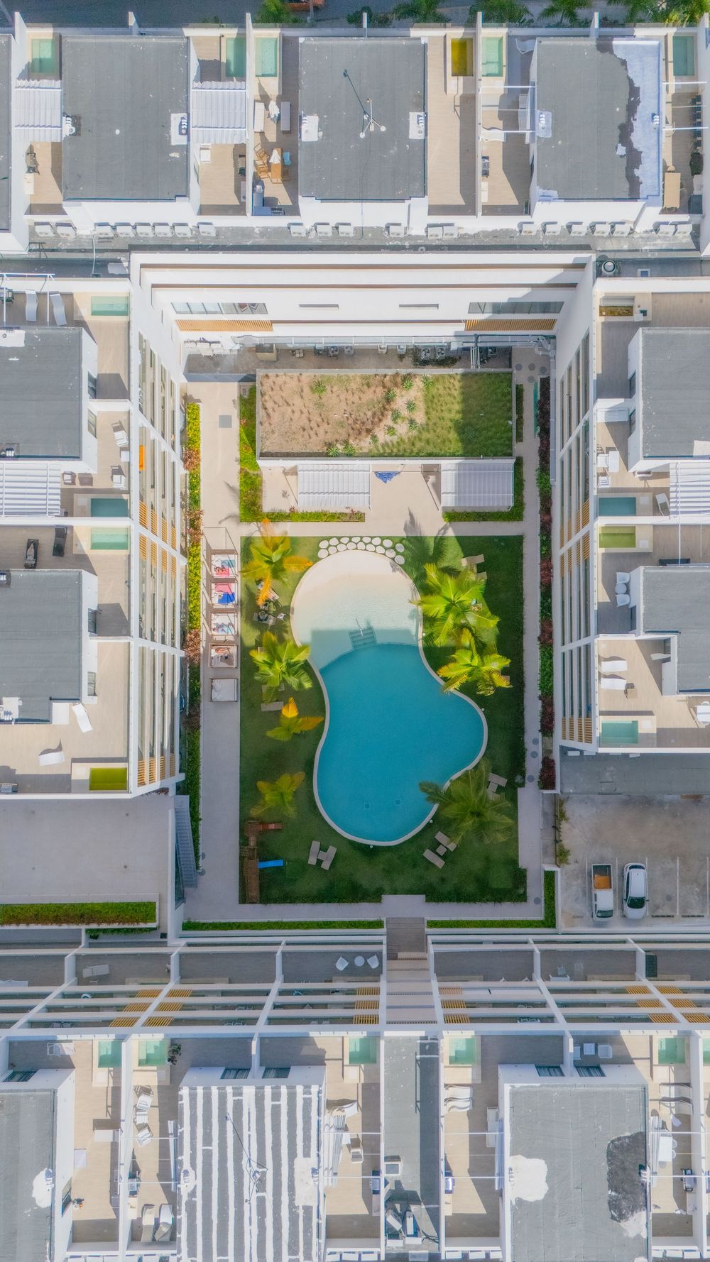 Aerial view of a curved swimming pool and garden courtyard surrounded by modern residential buildings in an urban setting.