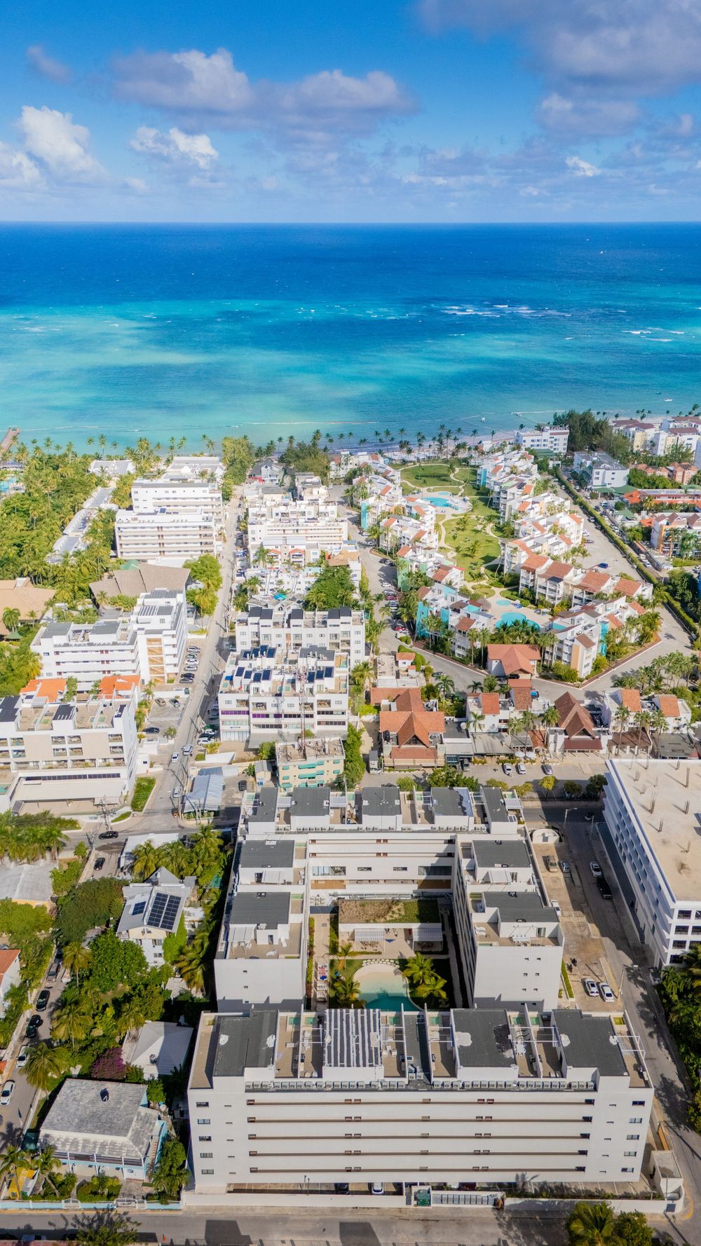 Aerial panoramic view of a coastal city with white buildings and turquoise ocean waters stretching to the horizon. Bavaro Real Este Photogra
