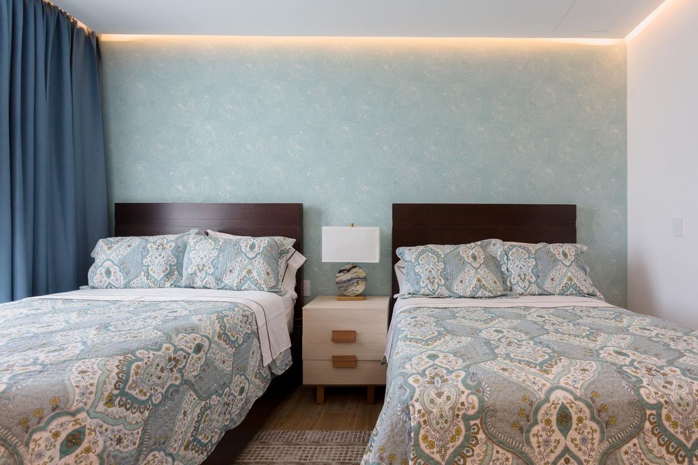 Two twin beds with blue paisley bedding flank a white nightstand in an elegant room with teal wallpaper.