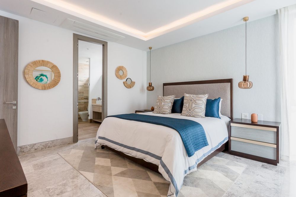 Elegant hotel bedroom with a queen bed, blue accents, pendant lights, marble floors, and an open bathroom door.