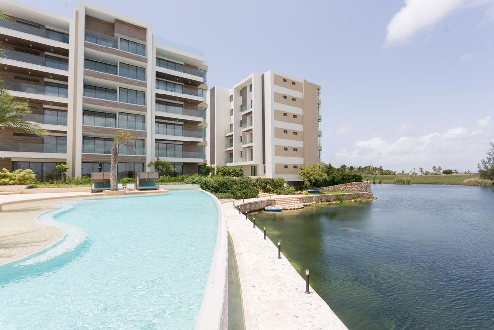 Modern waterfront condos with a resort-style pool overlooking a serene lagoon under clear blue skies.