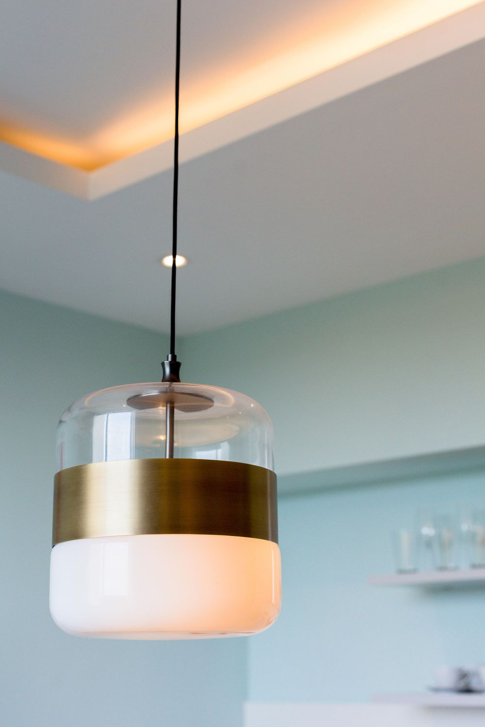 Contemporary pendant light with brass band and frosted glass shade hanging from ceiling in modern interior.