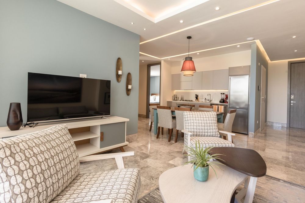 Modern open-plan living room with marble floors, wall-mounted TV, and a stylish kitchen dining area in neutral tones.