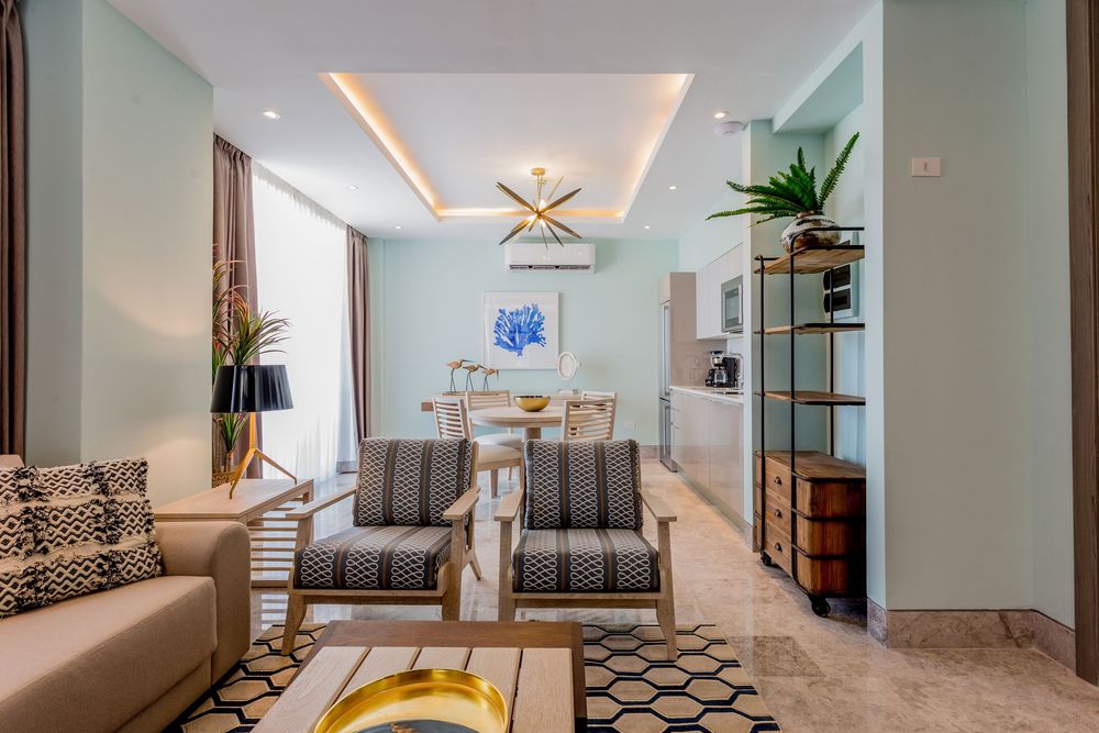 Modern living room with geometric patterned chairs, gold accents, teal walls, and open dining area in luxury apartment.