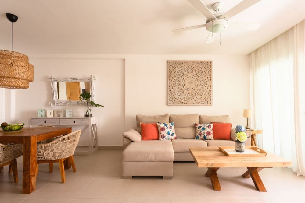 Modern minimalist living room with white walls, wooden furniture, and orange accent pillows features natural lighting. Real State.