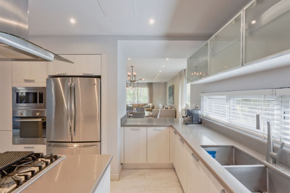 Modern white kitchen interior with sleek cabinets, stainless steel appliances and recessed lighting creates a bright cooking space. Real Sta