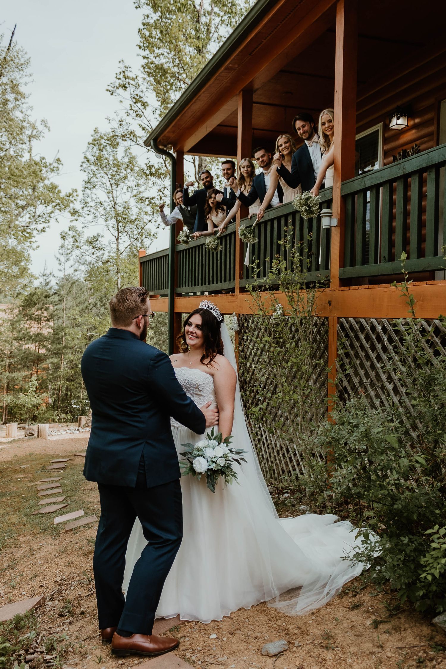 Wedding scene outside rustic cabin with guests watching from balcony.