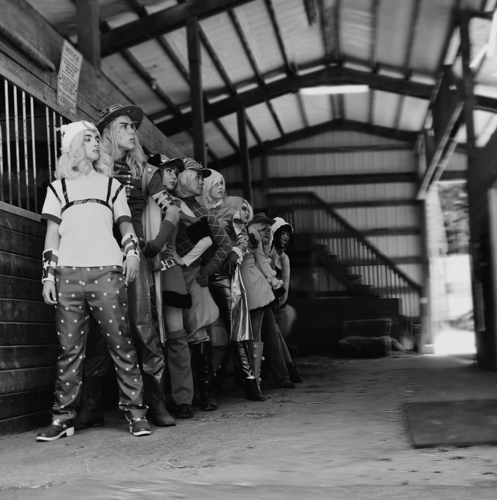 A line of people standing against a wall in what appears to be an indoor warehouse or industrial space.