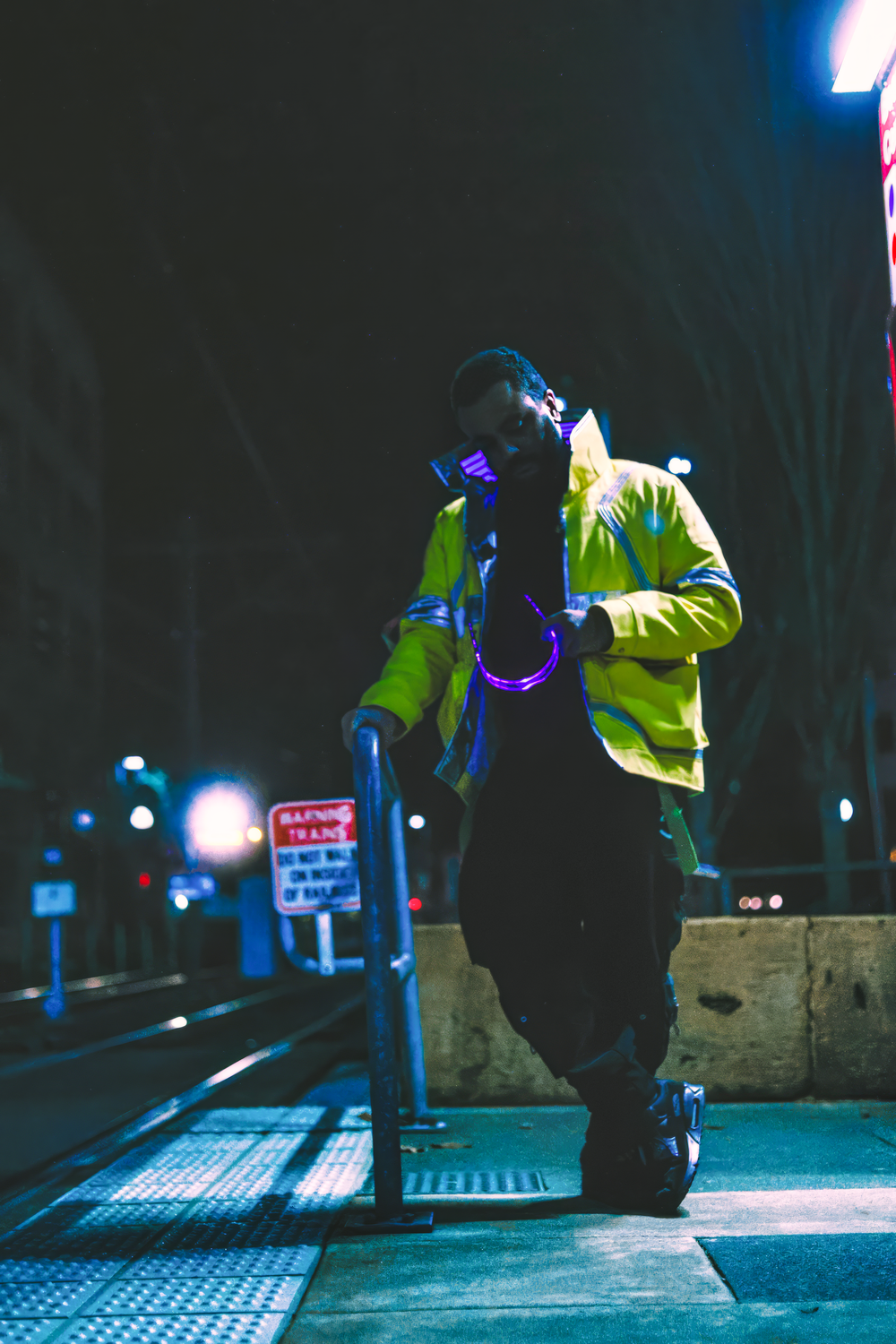 Person in neon yellow jacket performs dance moves on textured pavement at night under blue lighting.