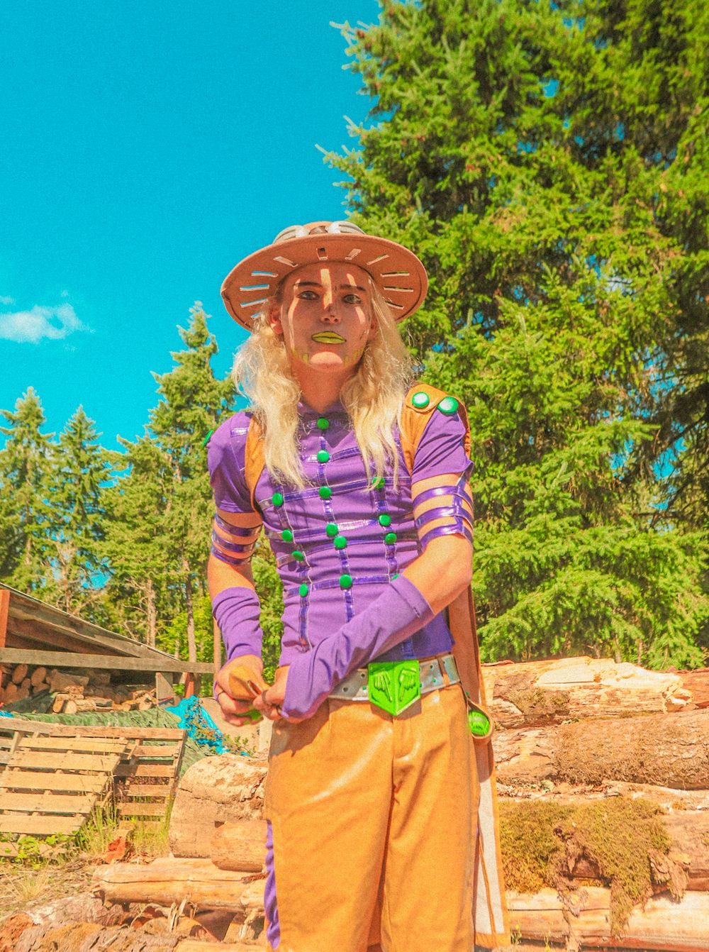 Person wearing purple striped shirt and tan hat enjoys outdoor hiking trail with evergreen trees and blue sky backdrop.