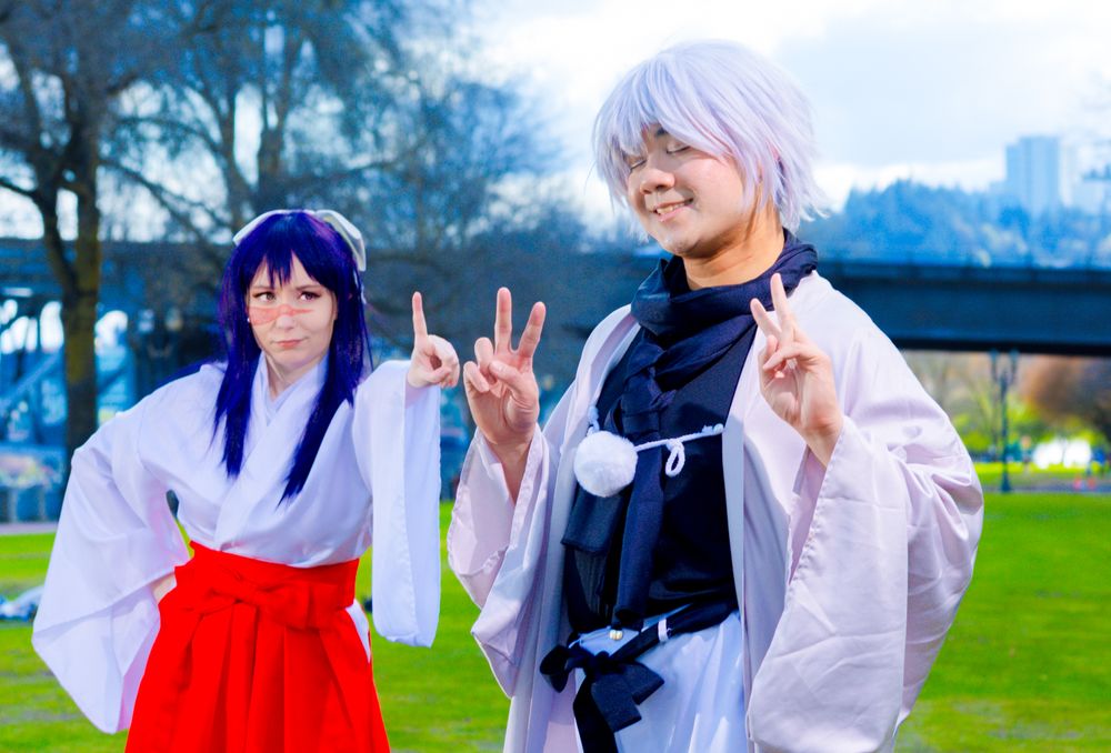 Cosplayers in traditional Japanese miko shrine maiden outfits with white tops and red hakama pose together outdoors.