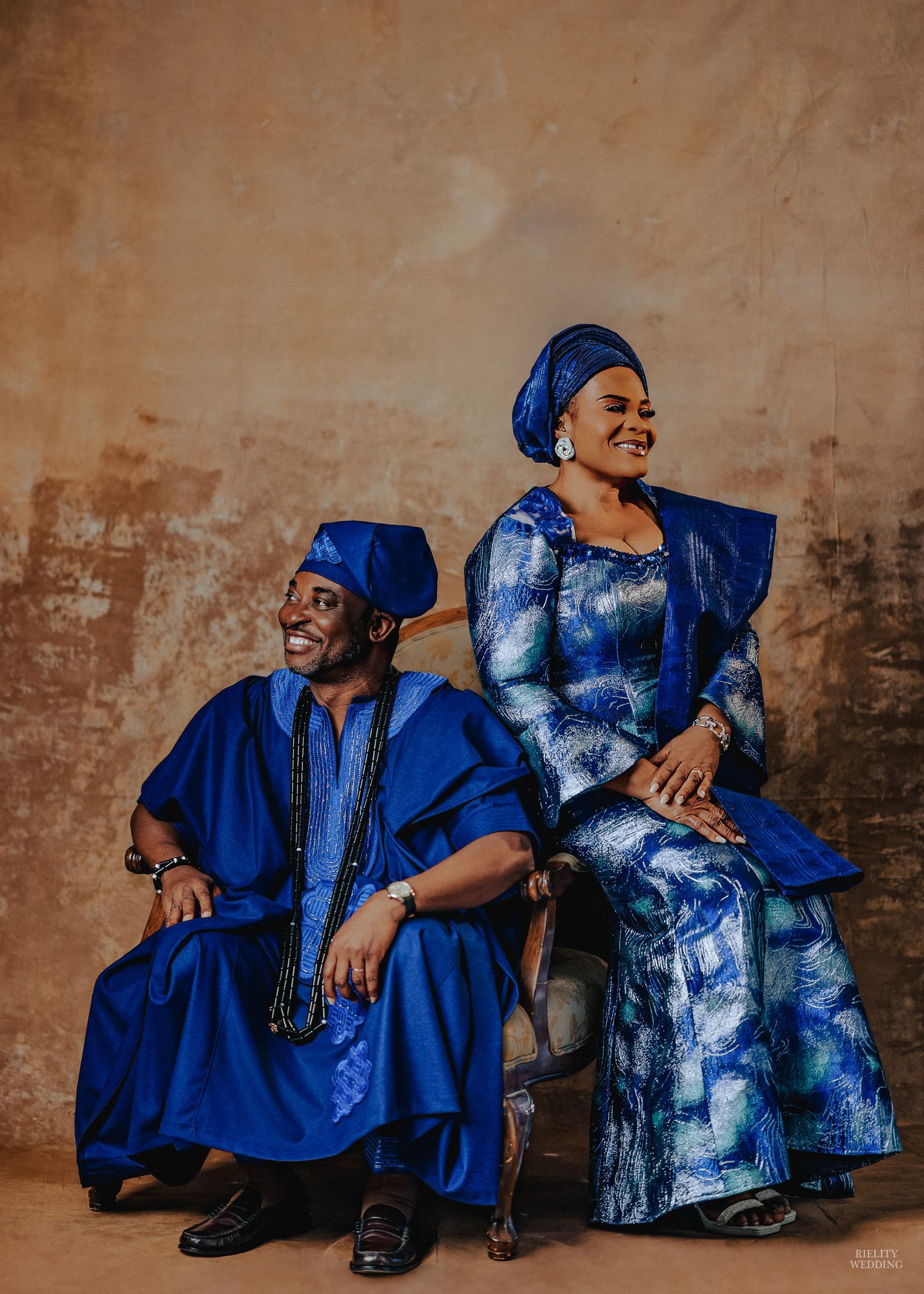 Couple in coordinating royal blue and tie-dye outfits pose playfully against a textured beige wall in a photo series.