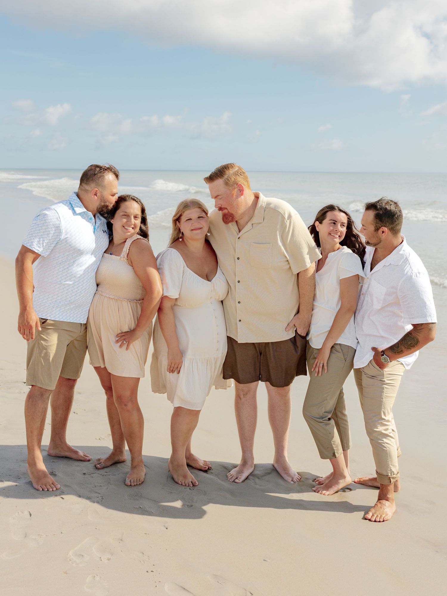 Group enjoying a casual beach photoshoot wearing light summer clothing on white sand.