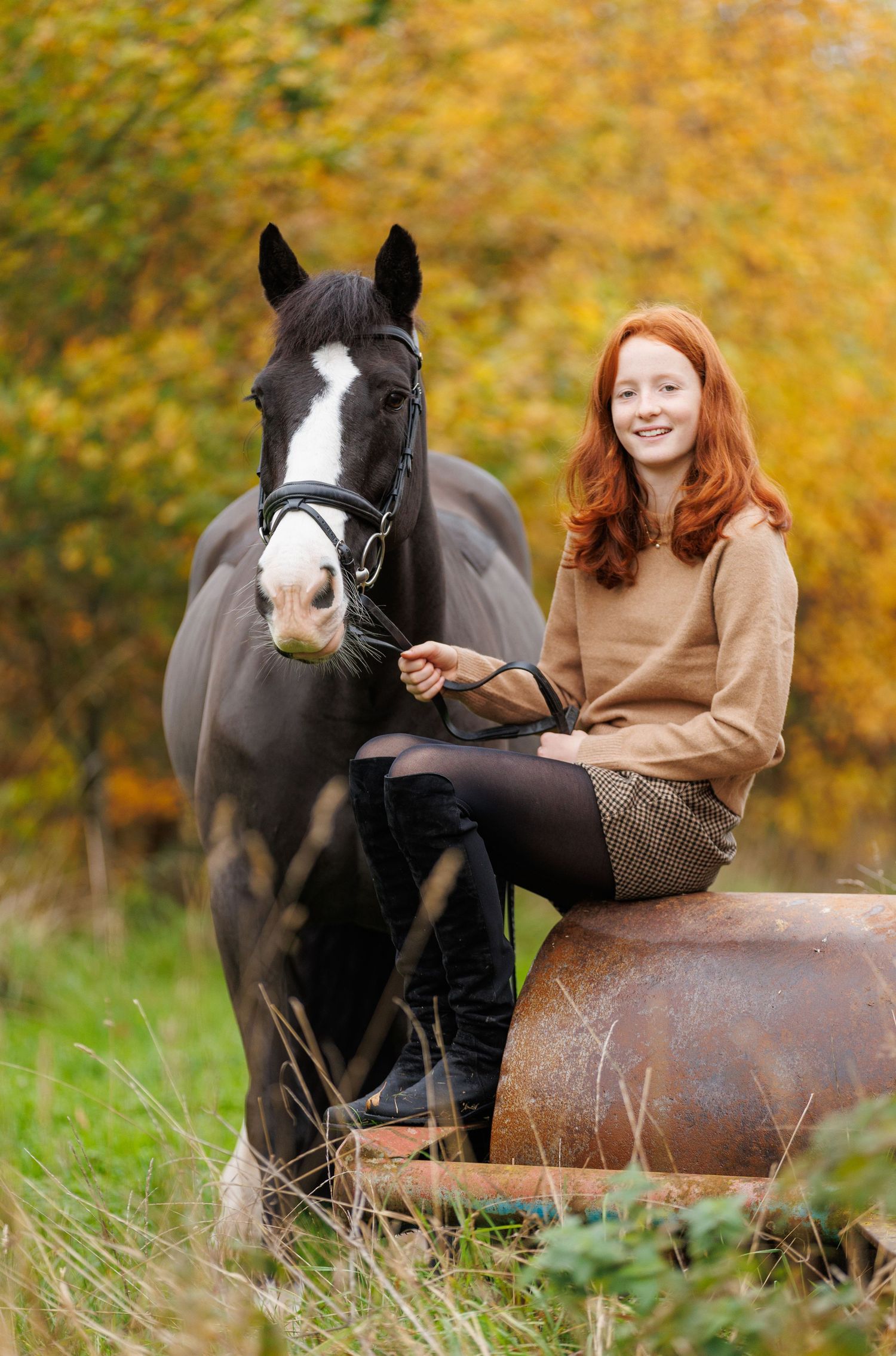 A beautiful bay horse wearing a black bridle stands next to someone in a white lace dress in an outdoor setting.