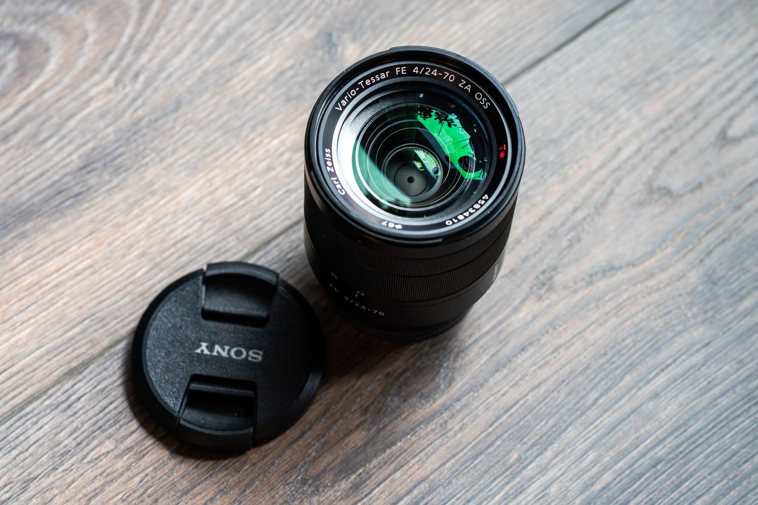 A black camera lens being disassembled on a wooden surface to show its internal components and mechanisms.