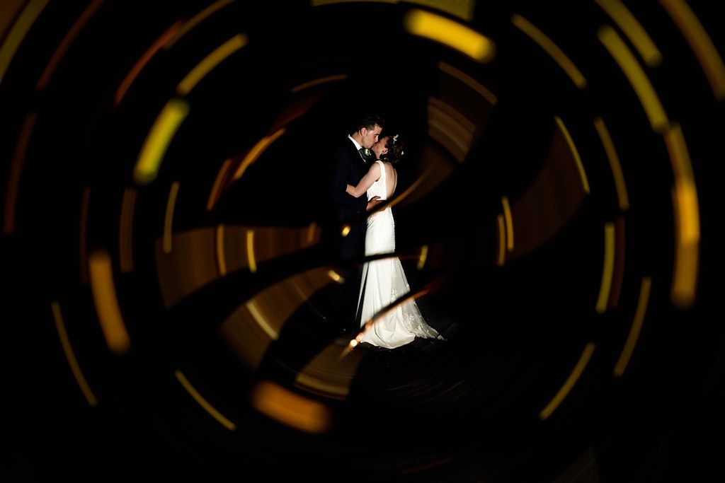 Bride and Groom kissing in the dark with a yellow light swirl around them at harefield Barn