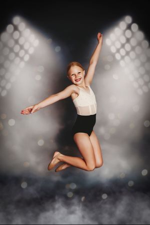 A dancer in white and black leaps through the air against a dark background with bokeh lighting effects.
Best child's photographer