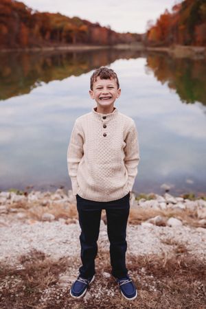 Child in cream sweater posing by lakeside with autumn reflections on water.

Best child's photographer
