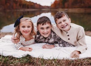 Family group lying on blanket during outdoor autumn photo-shoot with lake view.

Best photographer
