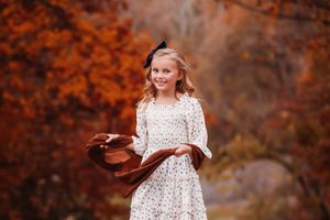 A girl in a floral dress twirls playfully in an autumn forest setting with warm orange foliage in the background.
Best child's photographer