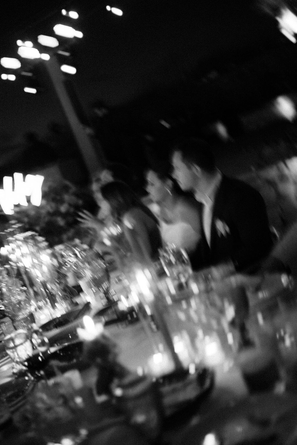 Blurred black and white nighttime photograph showing motion and lights at what appears to be a crowded venue or event.