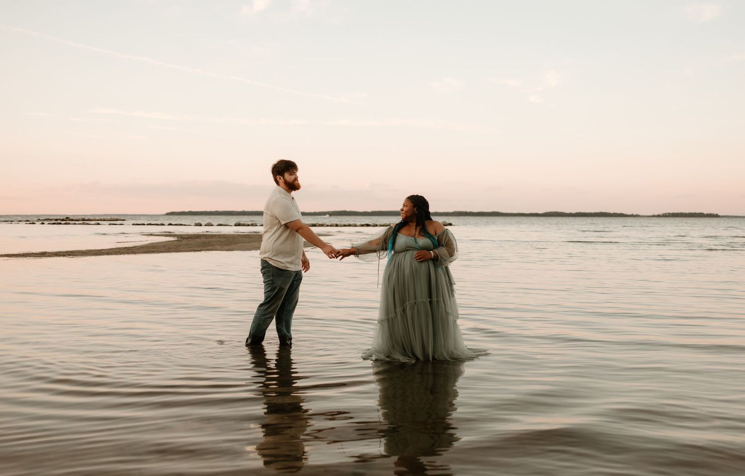 Romantic beach photoshoot at sunset with couple wading in calm ocean waters.