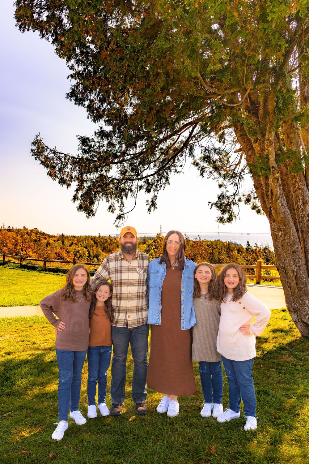 A group of people stand together under tall trees in a grassy field during golden hour.