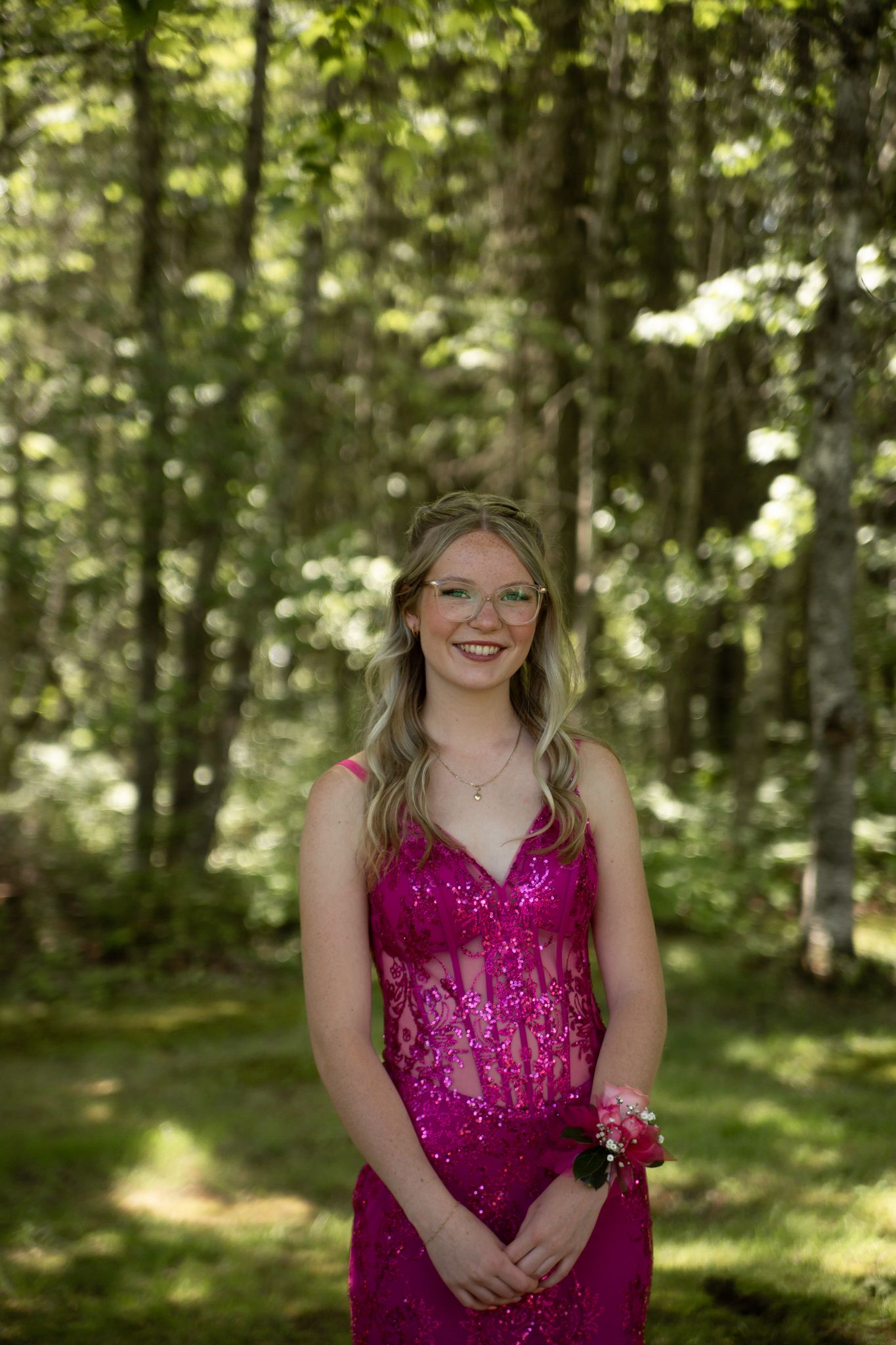 A sequined magenta formal dress sparkles in a serene wooded setting with dappled sunlight filtering through leaves.
