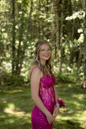 A formal portrait in a magenta sequin dress standing in a sunlit forest setting with dappled light through trees.